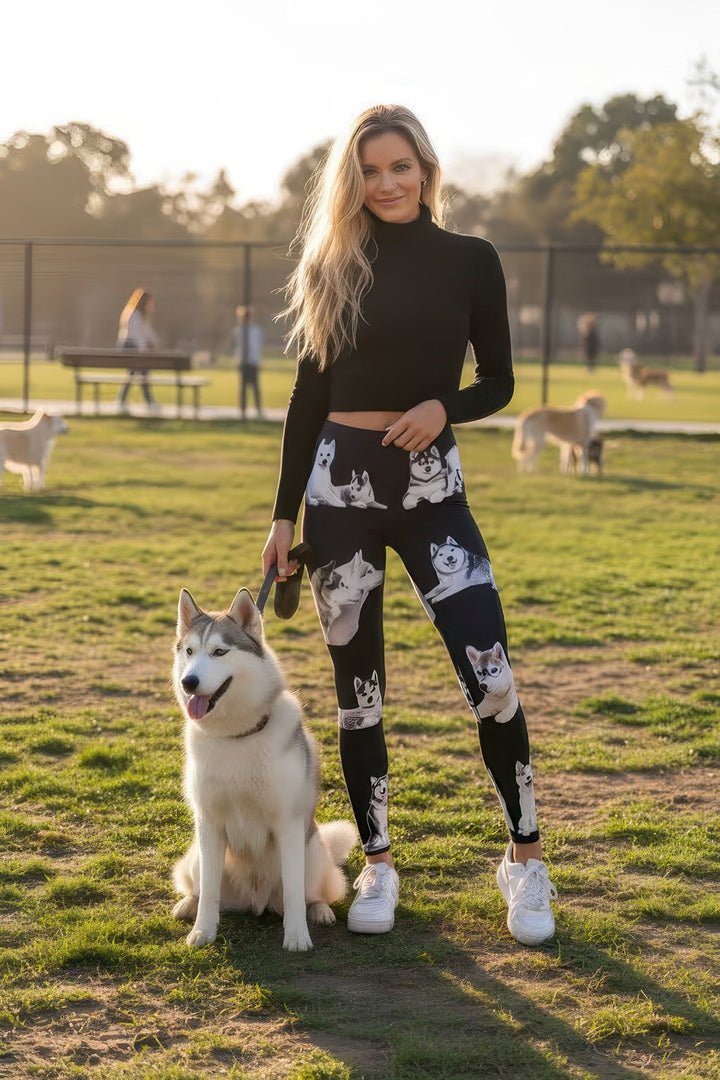 Woman with a real dog at a dog park wearing Denimaxx Alaskan Malamute print high-rise leggings, a black turtleneck, and white sneakers.