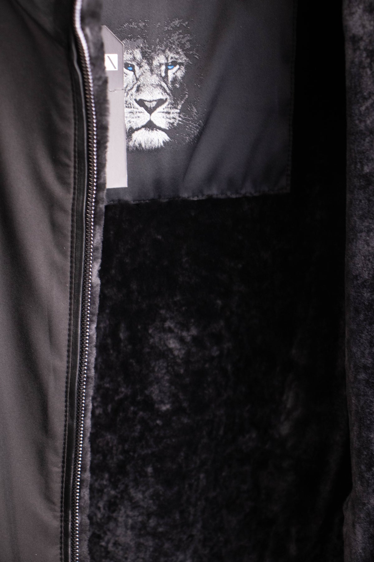 Close-up of the black nylon jacket opened to reveal the plush black shearling lining and lion logo label.