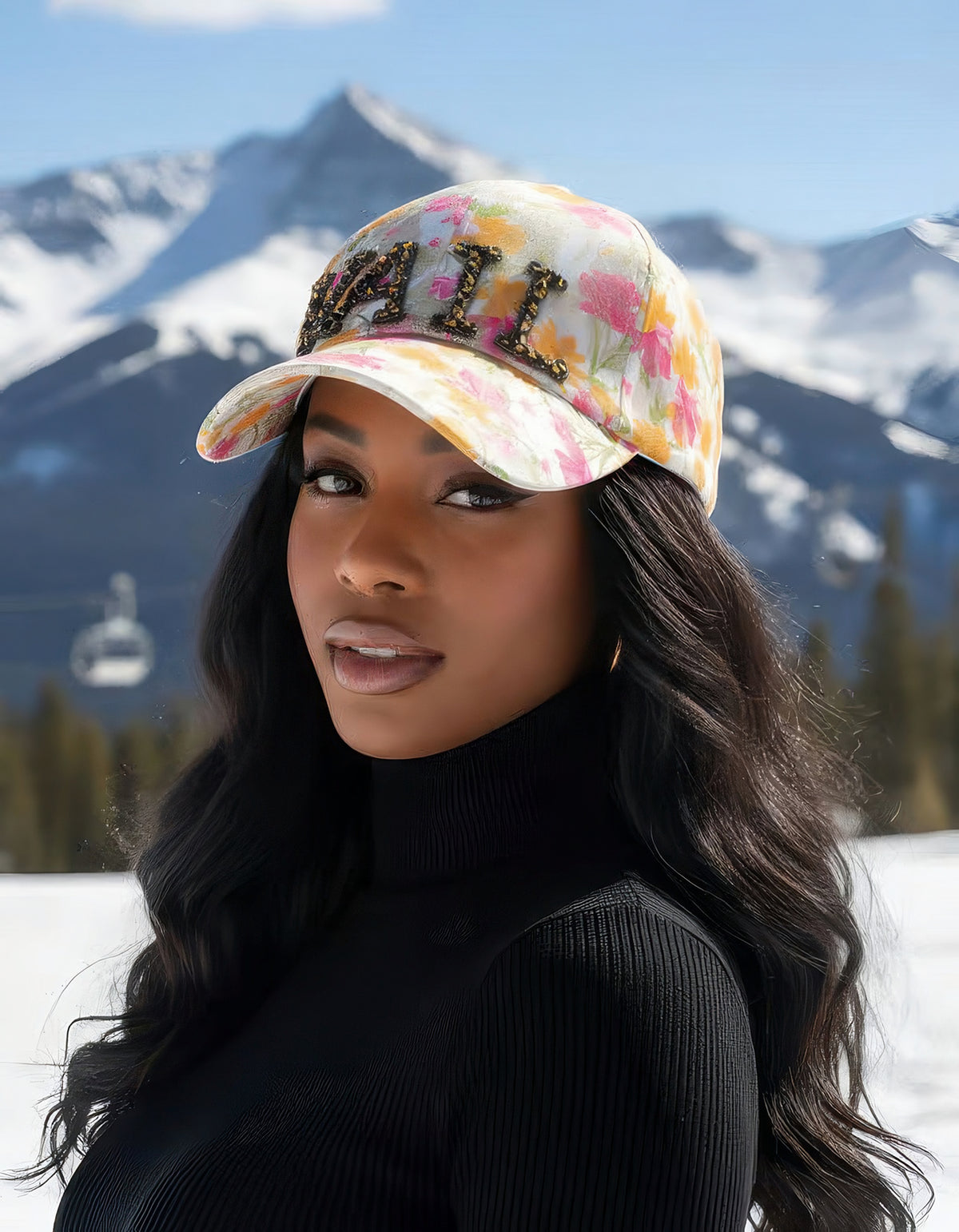 Woman wearing the Crystal-Embellished Vail baseball cap with crystal VAIL lettering on pink floral lace, snowy mountain backdrop.