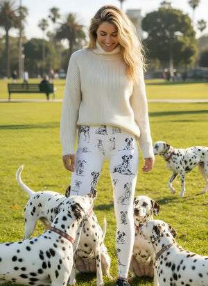 Woman in a white turtleneck sweater wearing Dalmatian print leggings, surrounded by real Dalmatians at a sunny park.