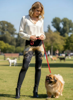 Woman in a white blouse wearing Pekingese print leggings with a large dog face across the thighs, holding a leash with a real Pekingese at the park.