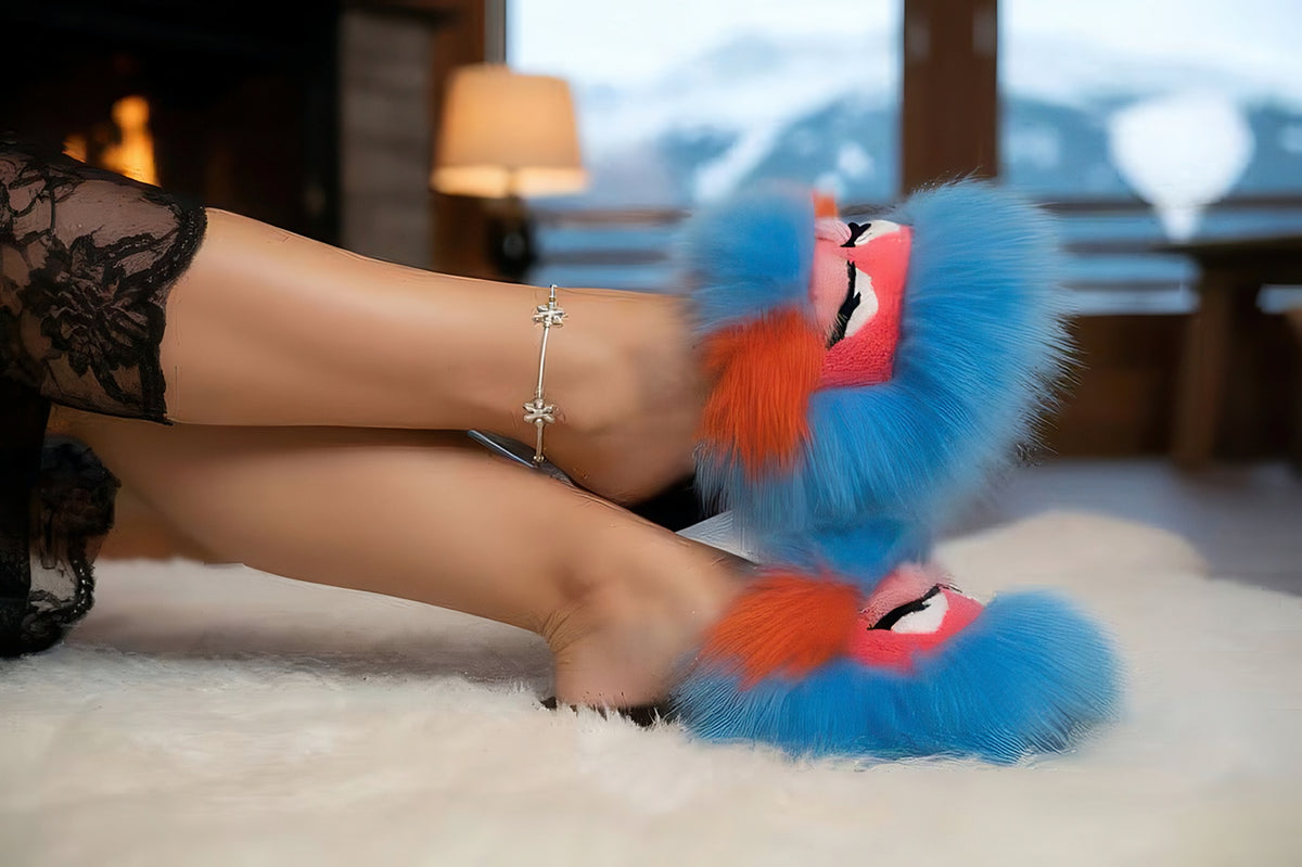 Womans legs in black lace loungewear wearing blue sheepskin slippers with pink monster-face fox trim, resting on a fur rug by the fireplace.