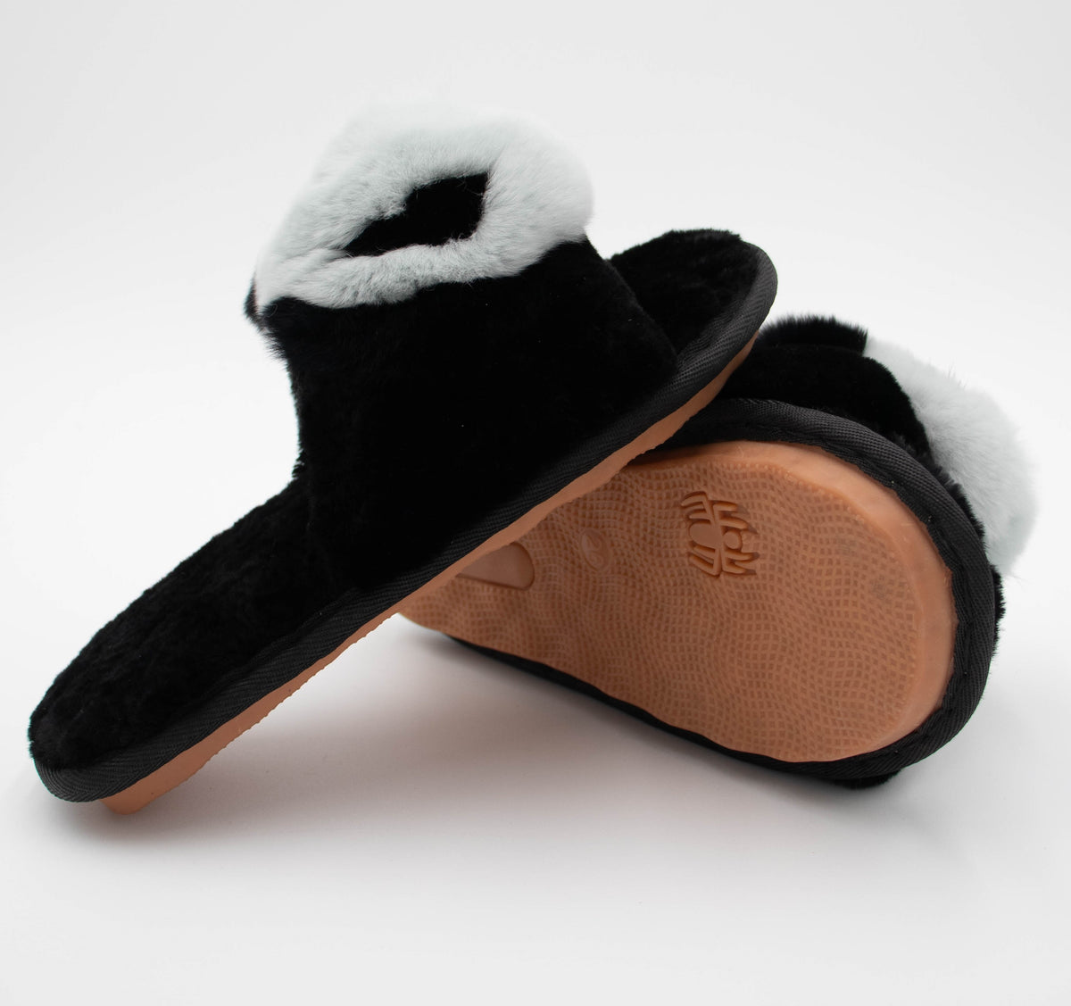 Black sheepskin slide slippers showing the tan rubber outsole with embossed logo, one slipper upright.