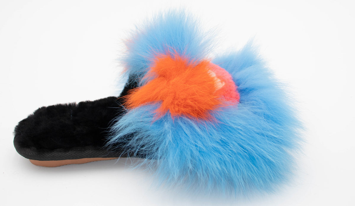 Side view of the blue sheepskin slide slipper with fluffy blue fox trim and orange and pink monster-face detail.