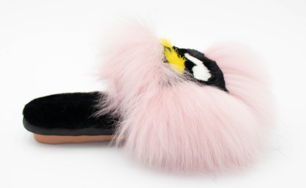 Side view of a single pink fox fur slide slipper with monster-eye embroidery and plush sheepskin footbed.