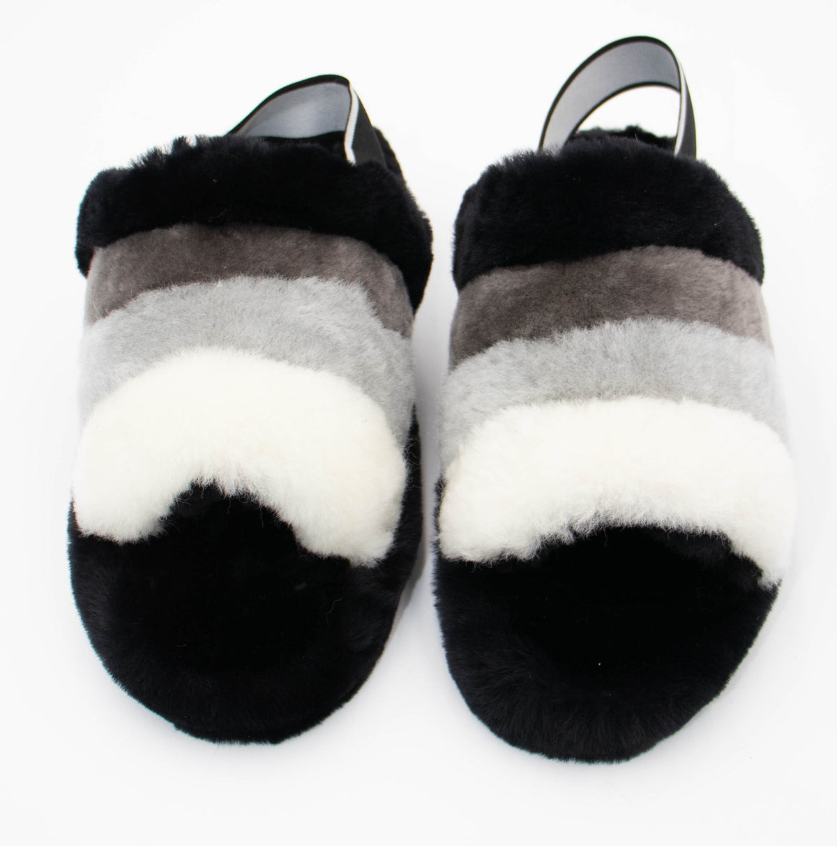 Top view of black sheepskin slide slippers with gray and white striped straps and black heel bands, studio shot.