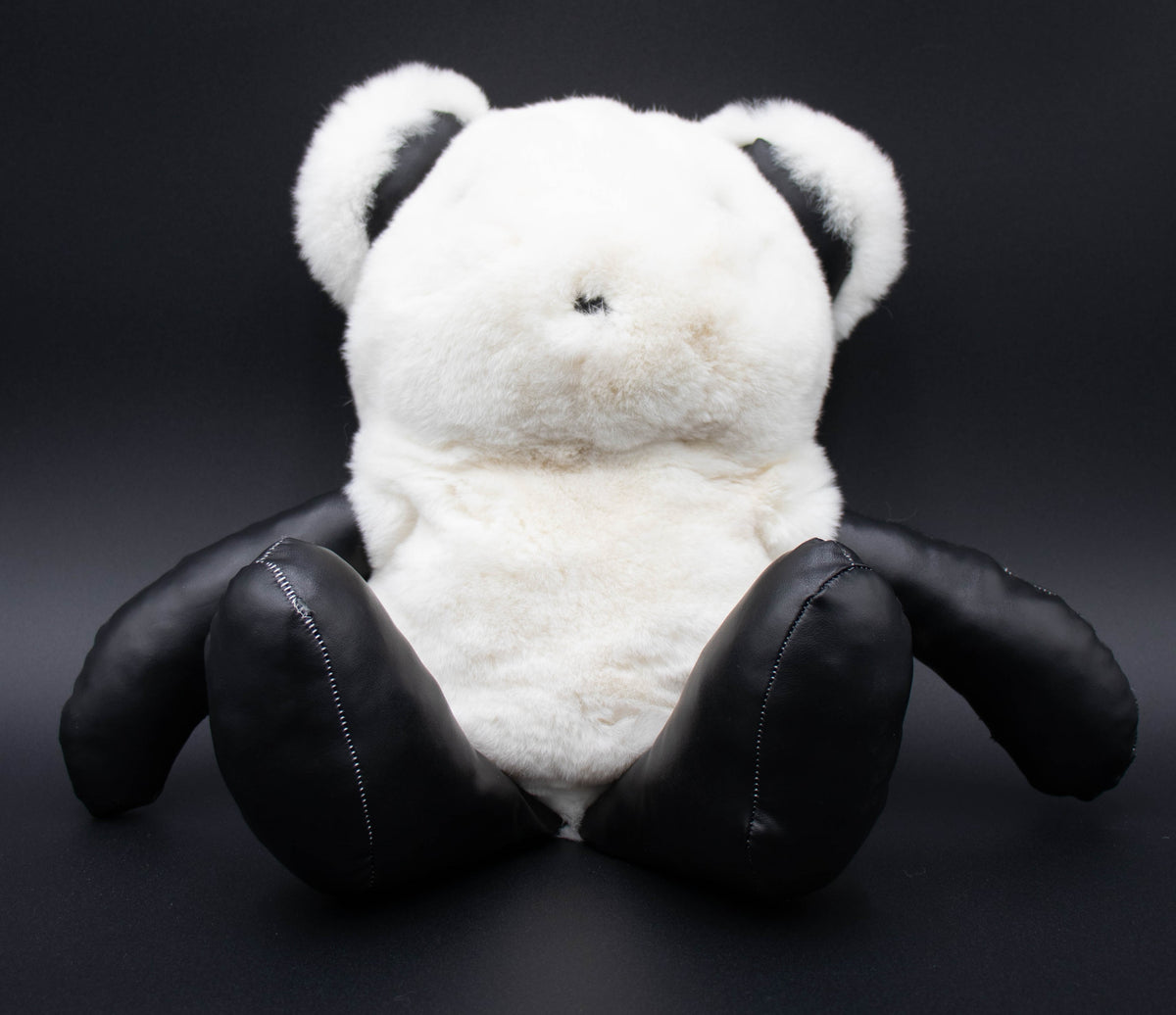 Front view of the white rex rabbit fur bear backpack with black leather arms and legs, studio shot on black.