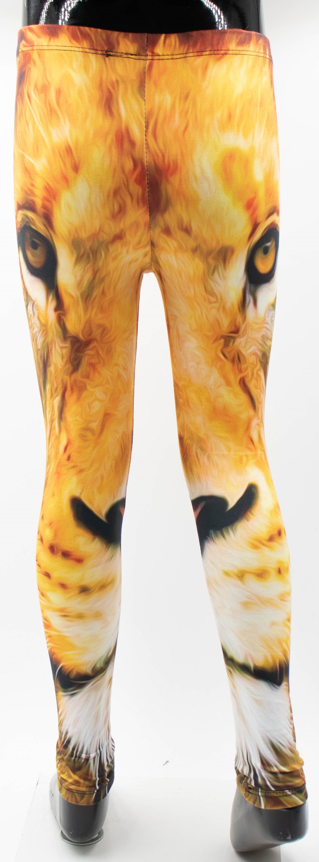 Back view of Denimaxx kids lion print leggings on a mannequin, golden lion face print with amber eyes across the upper legs, white studio background.