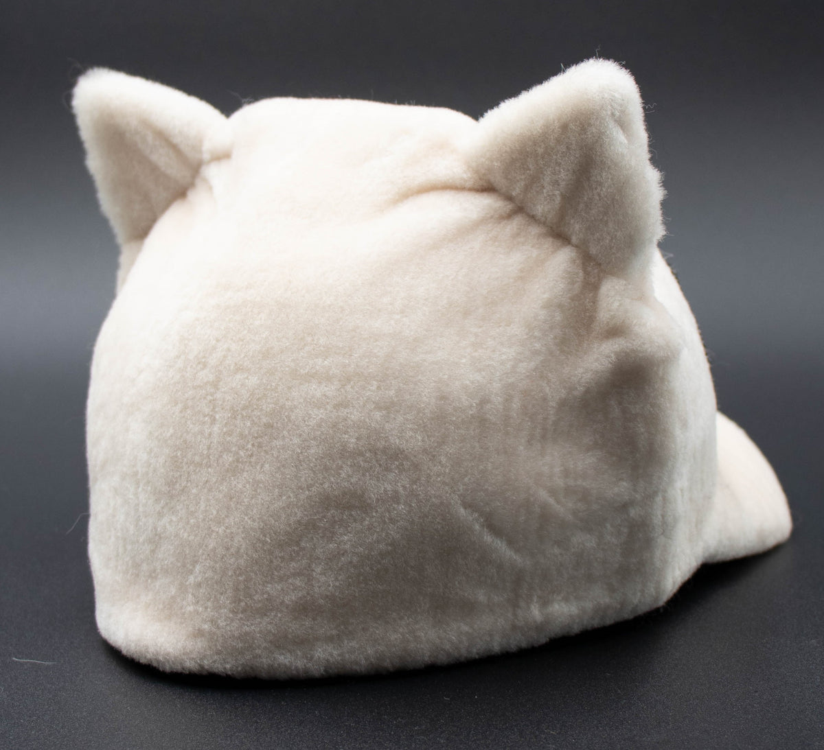 Back view of the white Apres Crystal cat ear winter hat showing the plush cat ears, on a dark background.