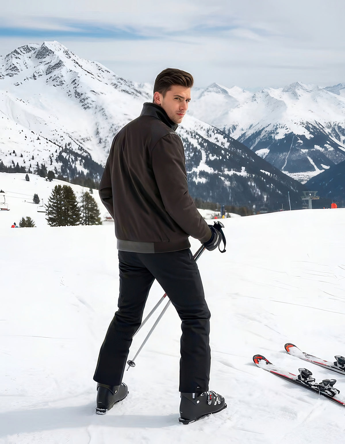 Back three-quarter view of man in the dark nylon shearling bomber jacket holding a ski pole, skis resting on snow with mountain panorama.