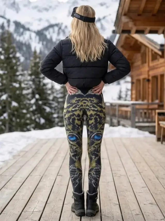 Back view of woman on a mountain lodge deck wearing Blue-Eyed Leopard Mosaic leggings showing the gold and green mosaic leopard with blue eyes on black.
