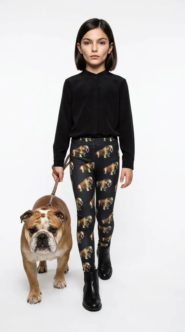 Girl in a black top and black boots walking an English Bulldog on a leash, wearing black kids leggings with an all-over Bulldog print
