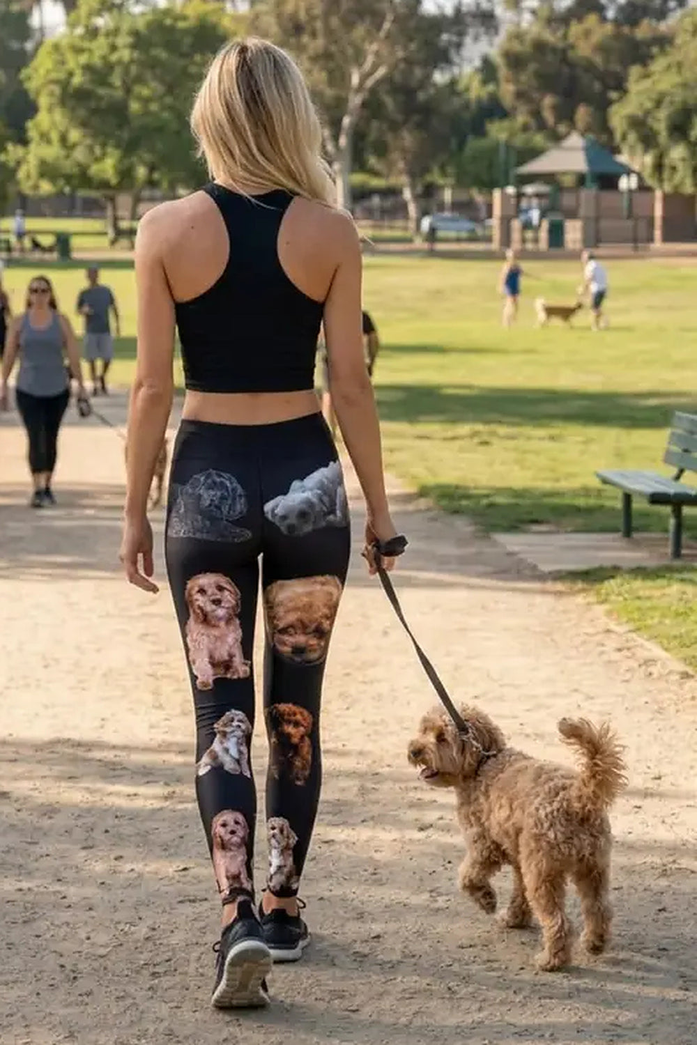 Back view of a woman walking an apricot cavapoo on a park path in black cavapoo print leggings