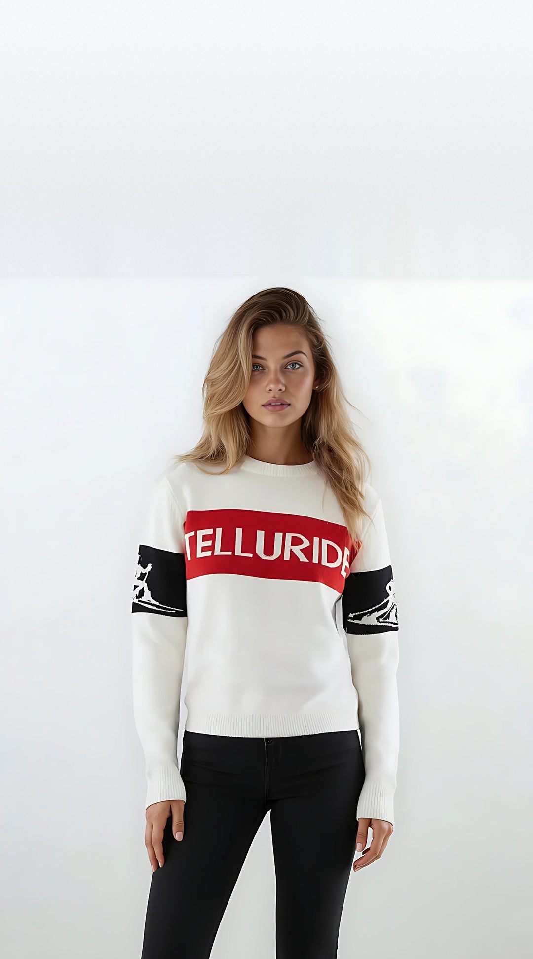 Woman modeling the white Telluride relaxed intarsia ski sweater with a red TELLURIDE chest band and black skier silhouette sleeve bands.