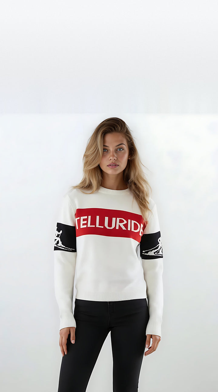 Woman modeling the white Telluride relaxed intarsia ski sweater with a red TELLURIDE chest band and black skier silhouette sleeve bands.