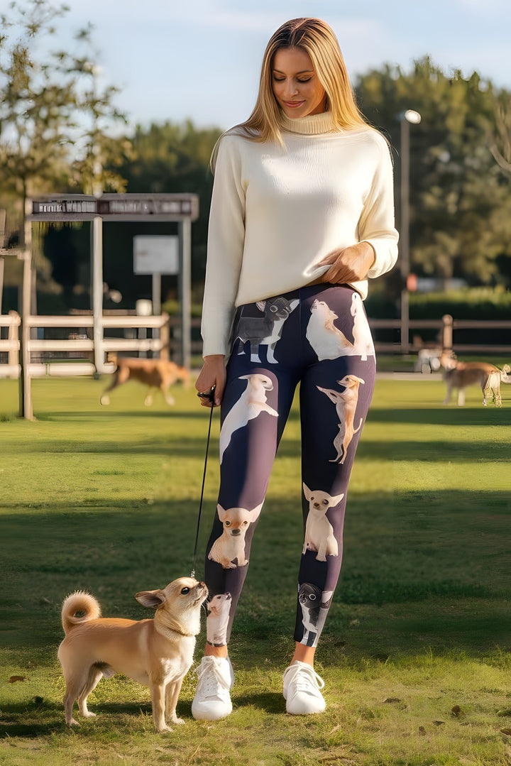 Woman in a cream turtleneck wearing Chihuahua print leggings, holding a leash with a real Chihuahua at the park.