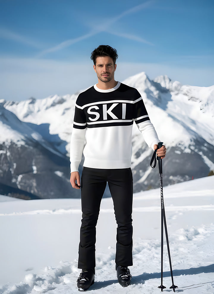 Man modeling the SKI intarsia crewneck sweater in black and white, holding a ski pole with snowy peaks behind.