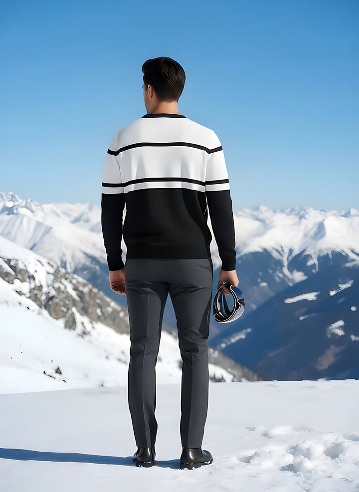 Back view of man wearing the black and white SKI intarsia crewneck sweater, holding goggles on a snowy peak.