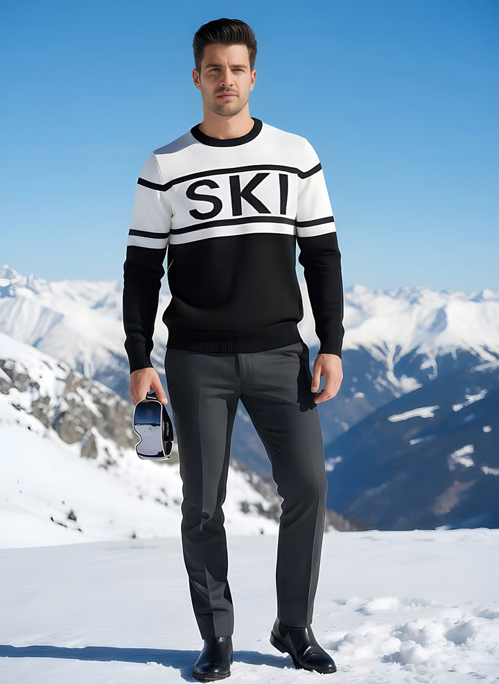 Man in the SKI intarsia crewneck sweater with black lettering on a white band, holding goggles in the snow.