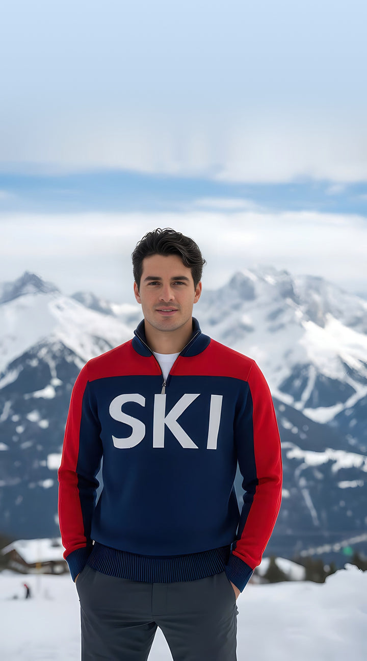 Man wearing the red, white, and navy SKI half-zip turtleneck ski sweater with hands in pockets on a snowy mountain.