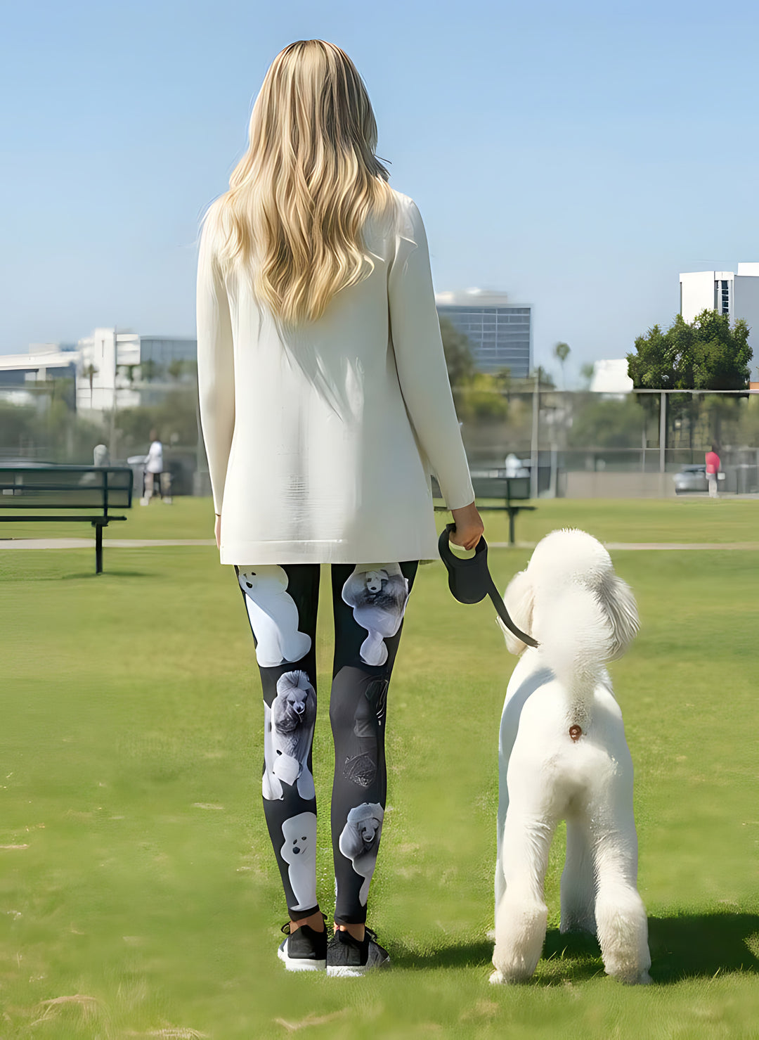 Back view of woman in Poodle print leggings and a white cardigan, walking a white Poodle on a leash in a park.