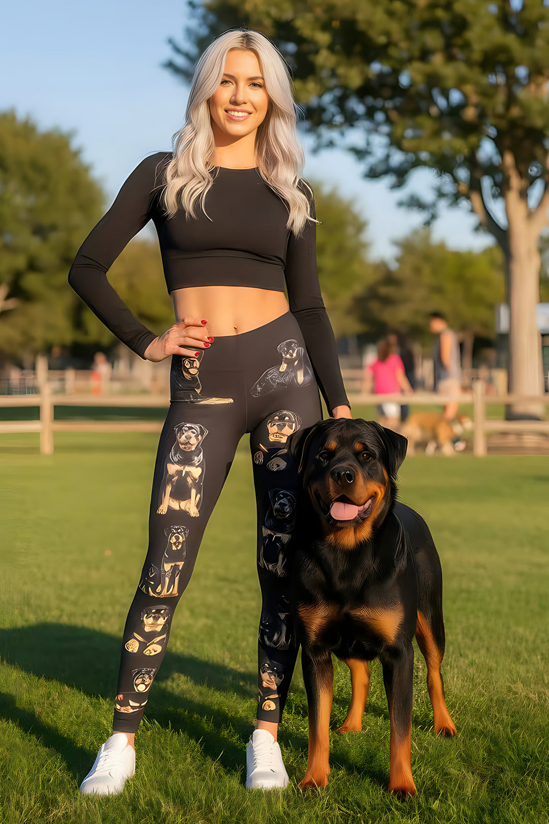 Woman wearing Rottweiler print leggings and a black crop top, standing beside a real Rottweiler in a park.
