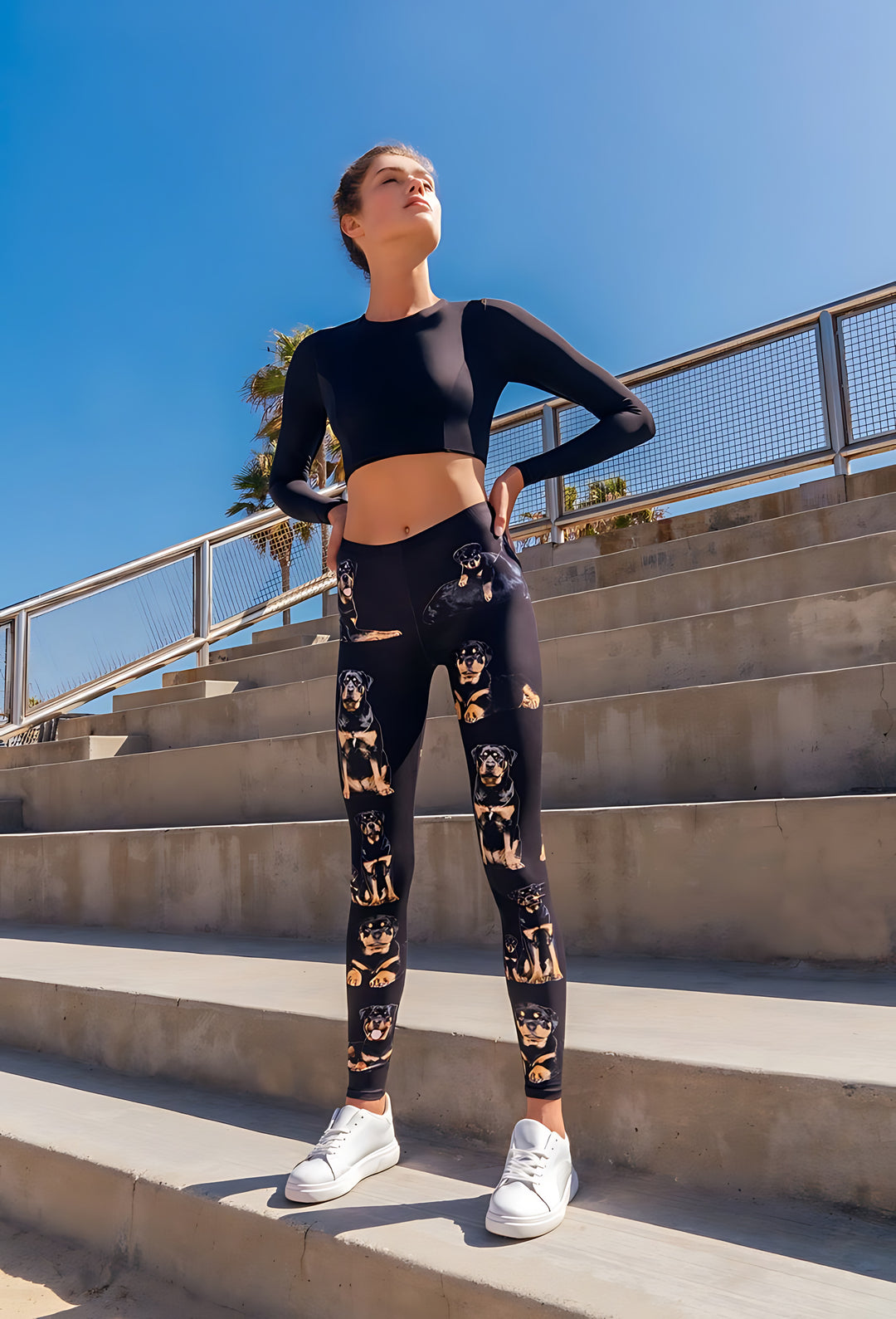 Woman modeling Rottweiler print leggings with a black crop top and white sneakers on concrete stadium steps.
