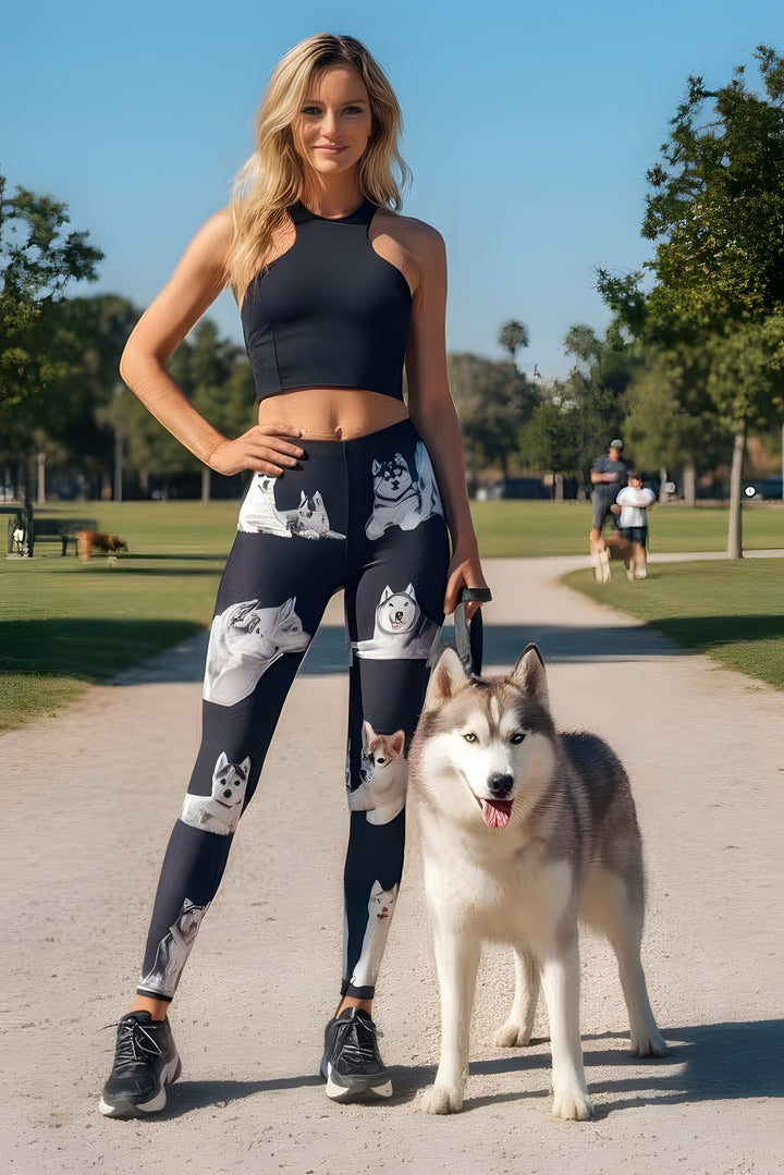 Woman wearing Siberian Husky print leggings and a black crop top, walking a real Husky on a park path.