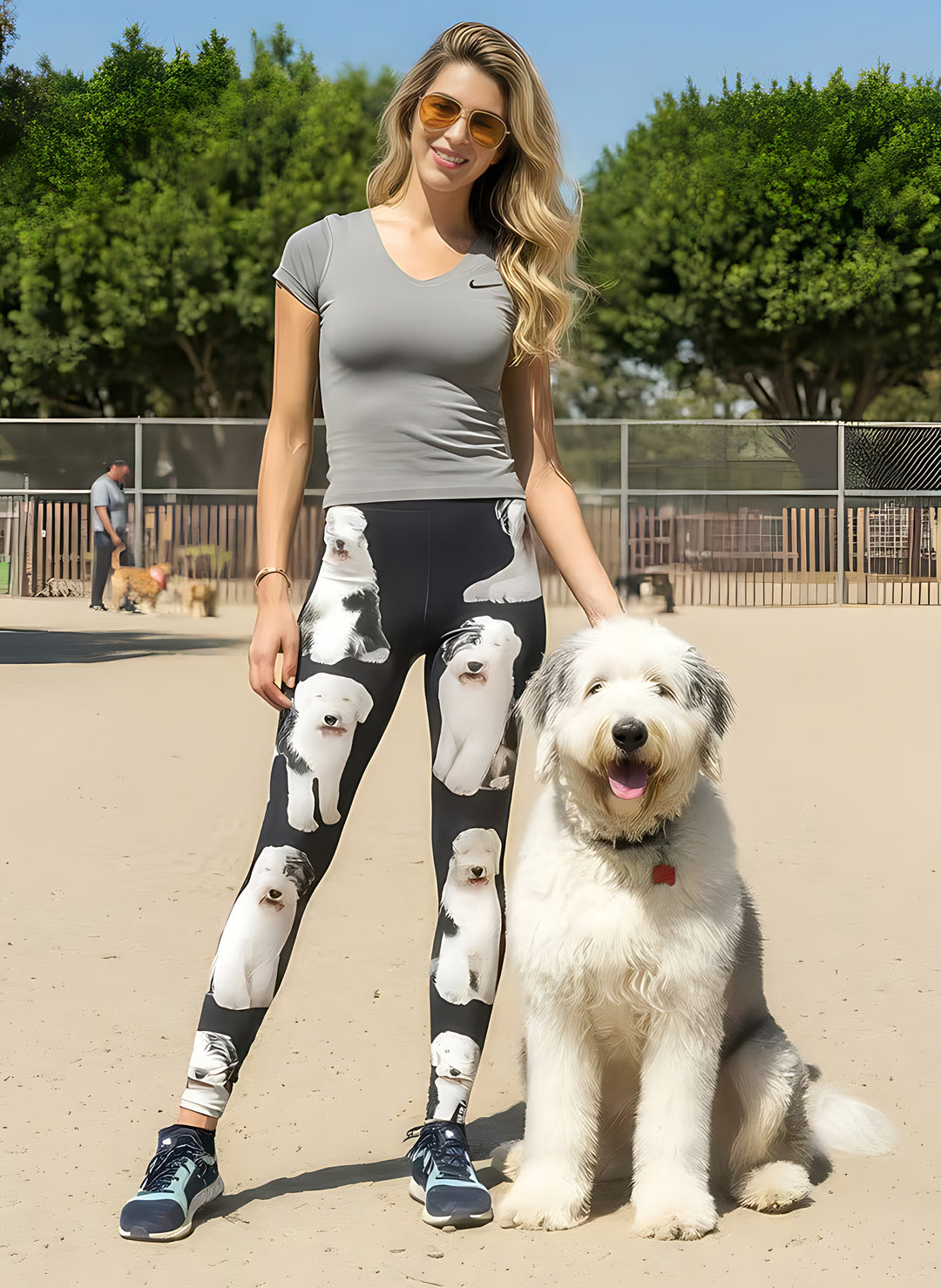 Woman wearing English Sheepdog print leggings and sunglasses, standing beside a real Old English Sheepdog at a dog park.