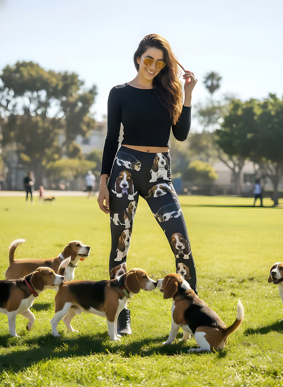 Smiling woman in sunglasses surrounded by real beagles on green grass, wearing Beagle print leggings with playful beagle artwork.