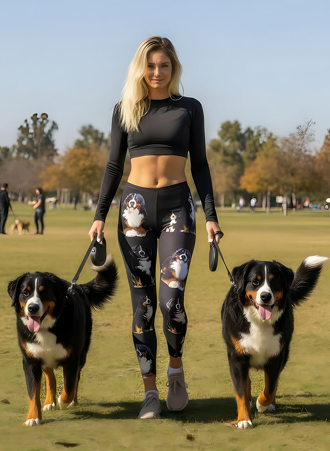 Woman walking two Bernese Mountain Dogs on leashes in a park, wearing Bernese Mountain Dog print leggings with realistic dog portraits.