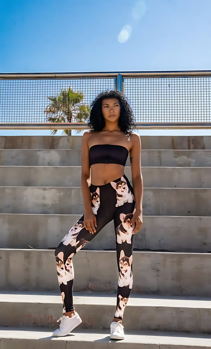 Woman with curly dark hair posing on concrete steps with palm trees behind, wearing Corgi print leggings and a black strapless sports bra.