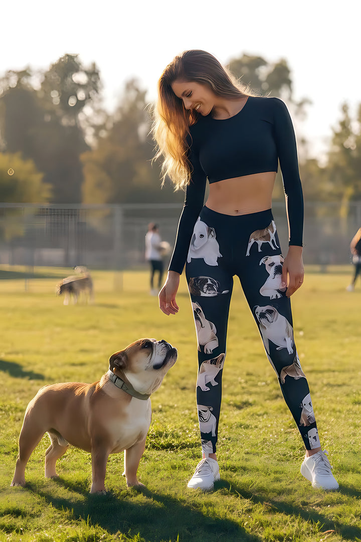 Woman smiling down at a real English bulldog while wearing English Bulldog print leggings and a black crop top in a sunny field.