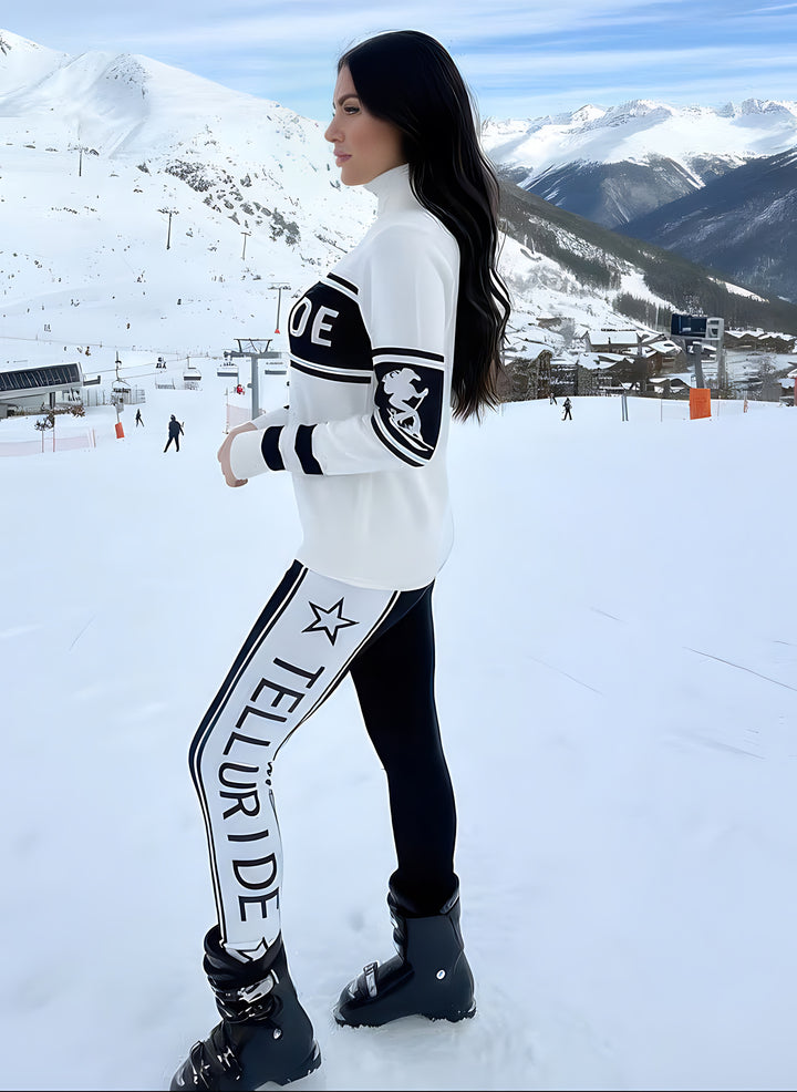 Side view of woman on a snowy slope wearing Telluride print leggings with TELLURIDE lettering and a star down the white side panel, paired with a white Telluride ski sweater.