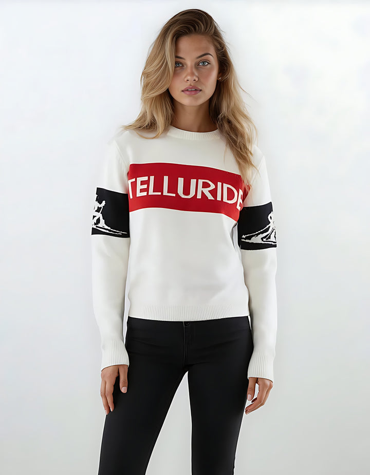 Woman modeling the white Telluride relaxed intarsia ski sweater with a red TELLURIDE chest band and black skier silhouette sleeve bands.