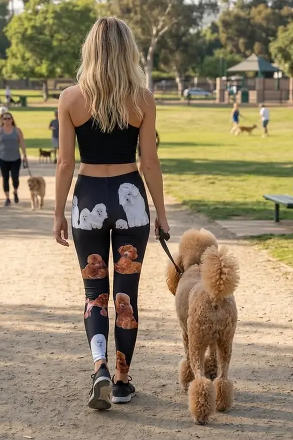 Back view of a woman walking an apricot standard poodle on a park path in fancy poodle print leggings