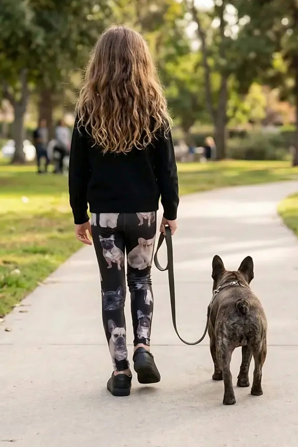 Back view of a girl walking a brindle French bulldog on a park path in French bulldog print girls leggings