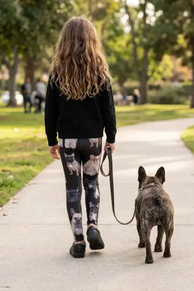 Back view of a girl walking a brindle French bulldog on a park path in French bulldog print girls leggings