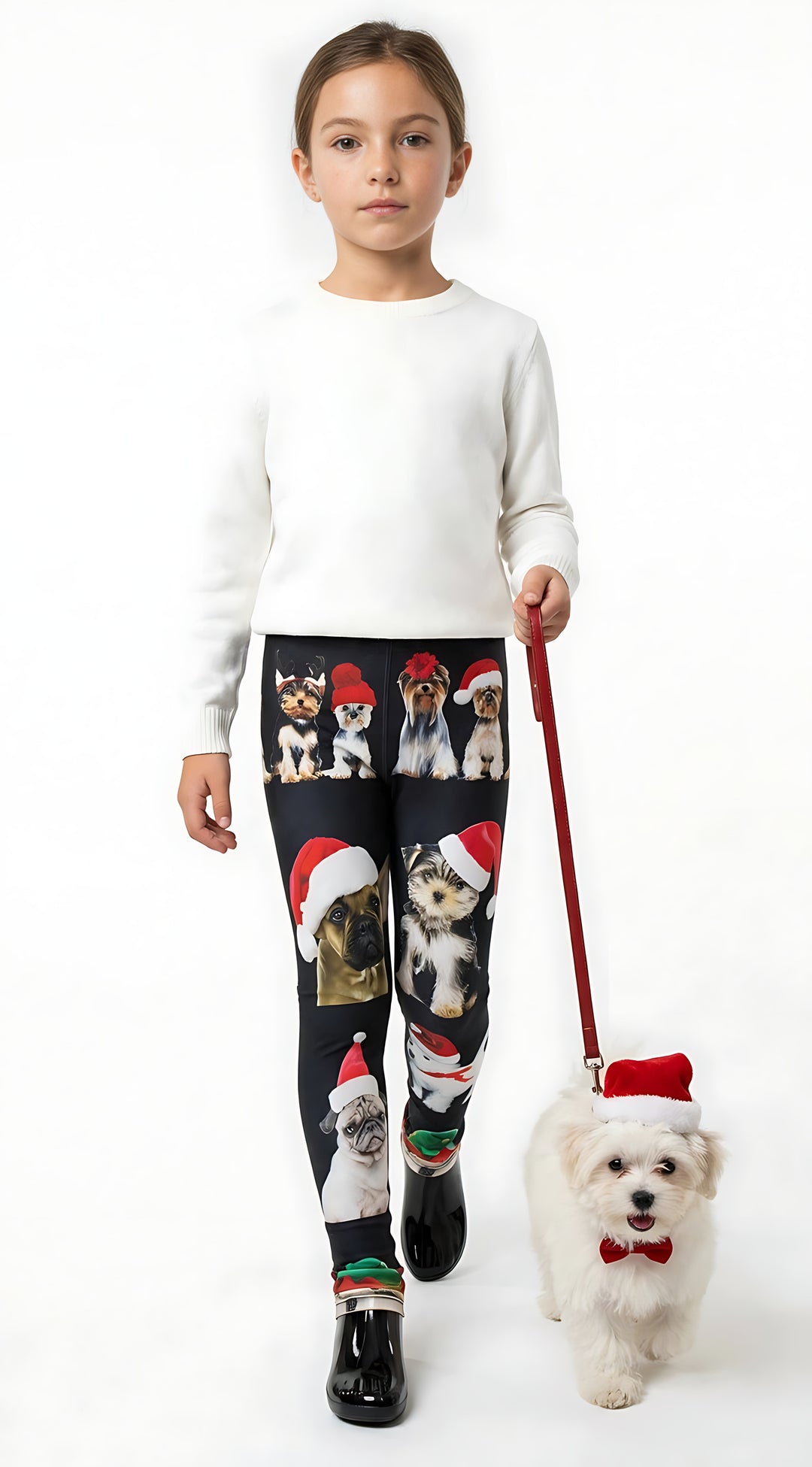 Young girl holding a leash with a small white dog in a Santa hat, wearing kids Christmas dogs print leggings and a white sweater.