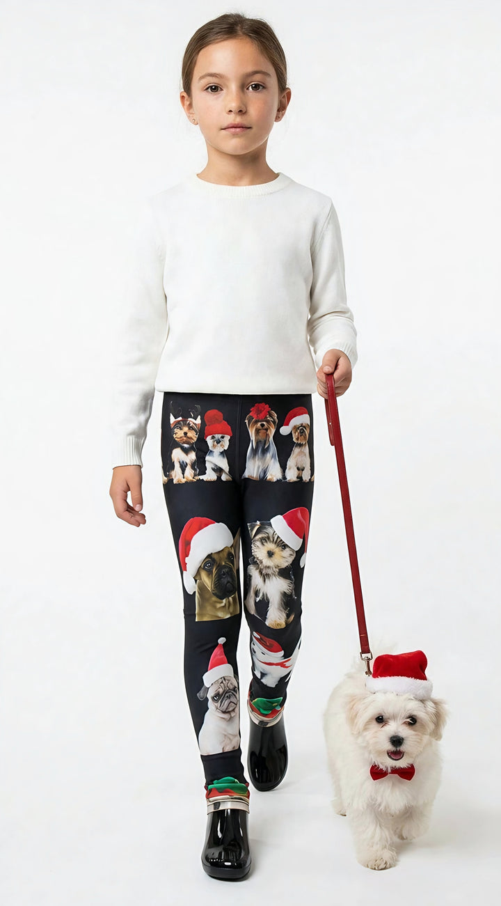 Young girl holding a leash with a small white dog in a Santa hat, wearing kids Christmas dogs print leggings and a white sweater.