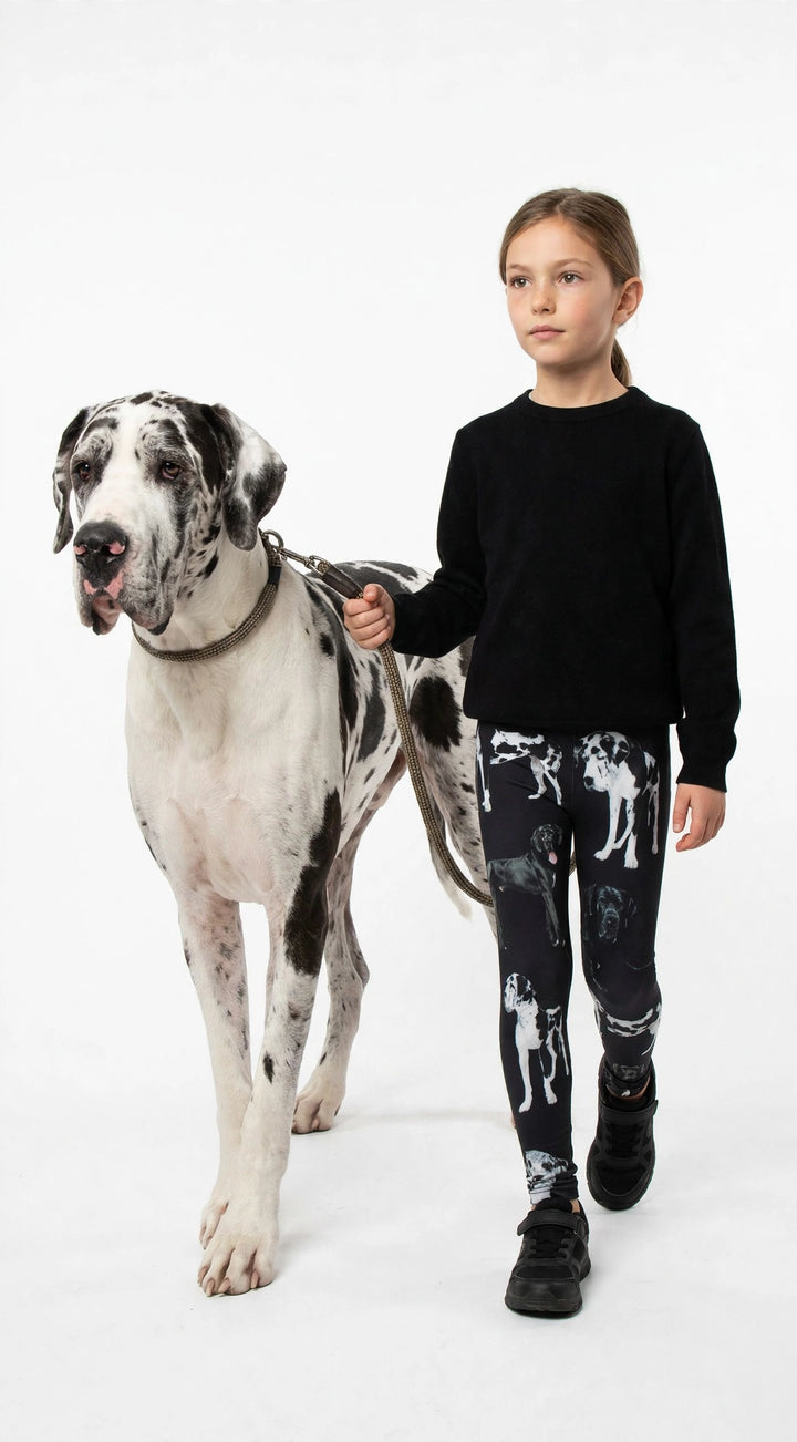 Young girl holding a leash with a real Great Dane, wearing Denimaxx kids Great Dane print leggings and a black top, studio shot.