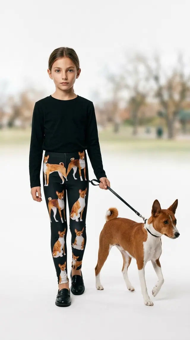Young girl in a white tank top standing on a patio with a Basenji dog, wearing black kids leggings with an all-over Basenji print
