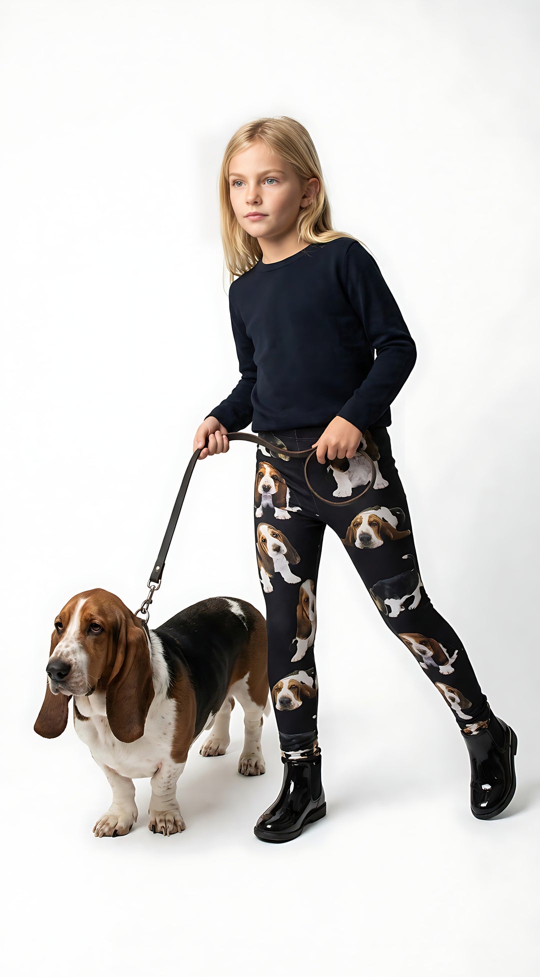 Young girl walking a real Basset Hound on a leash, wearing kids Basset Hound print leggings with puppy prints, black boots, white studio.
