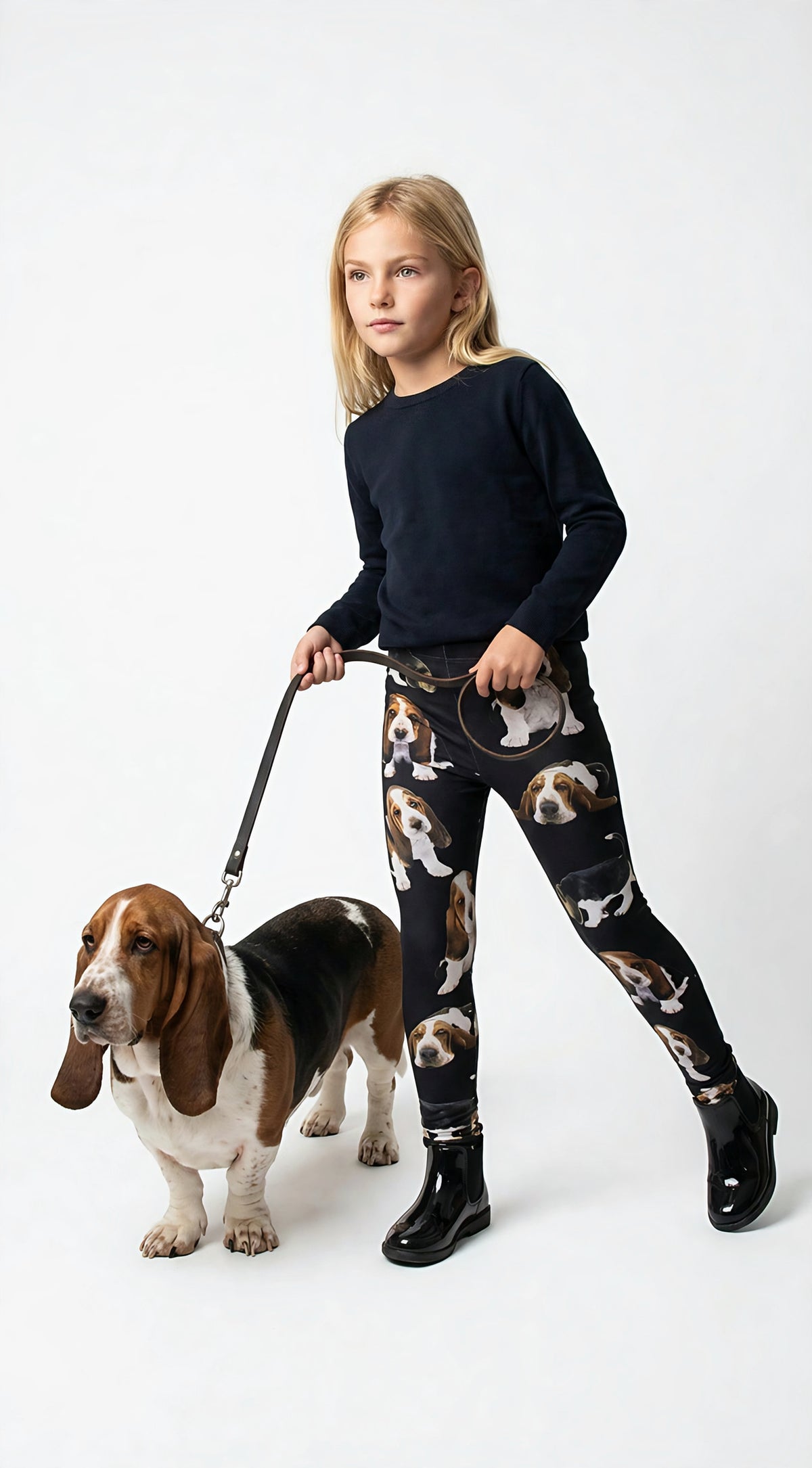 Young girl walking a real Basset Hound on a leash, wearing kids Basset Hound print leggings with puppy prints, black boots, white studio.