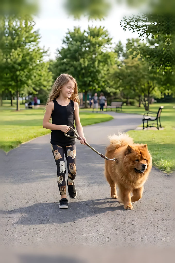 Girl in a black tank top walking a red Chow Chow in a park, wearing black Chow Chow puppy print girls leggings