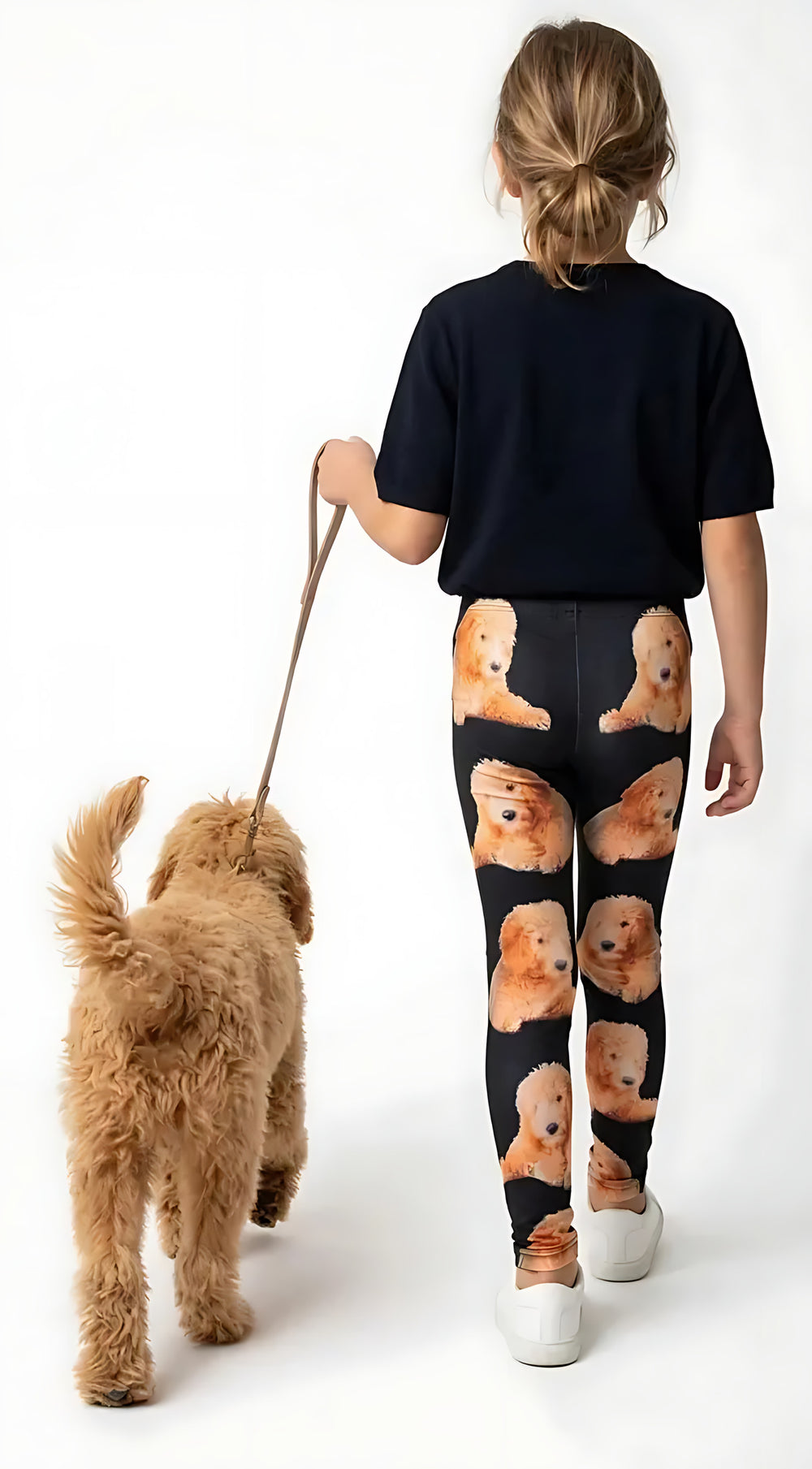 Back view of a girl in a navy tee walking a Goldendoodle, wearing black Goldendoodle print girls leggings