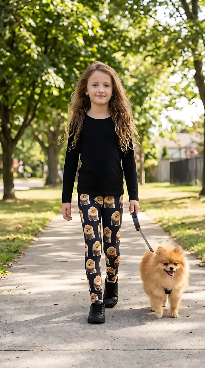 Girl in a black long-sleeve top walking a Pomeranian on a tree-lined sidewalk, wearing black Pomeranian print girls leggings