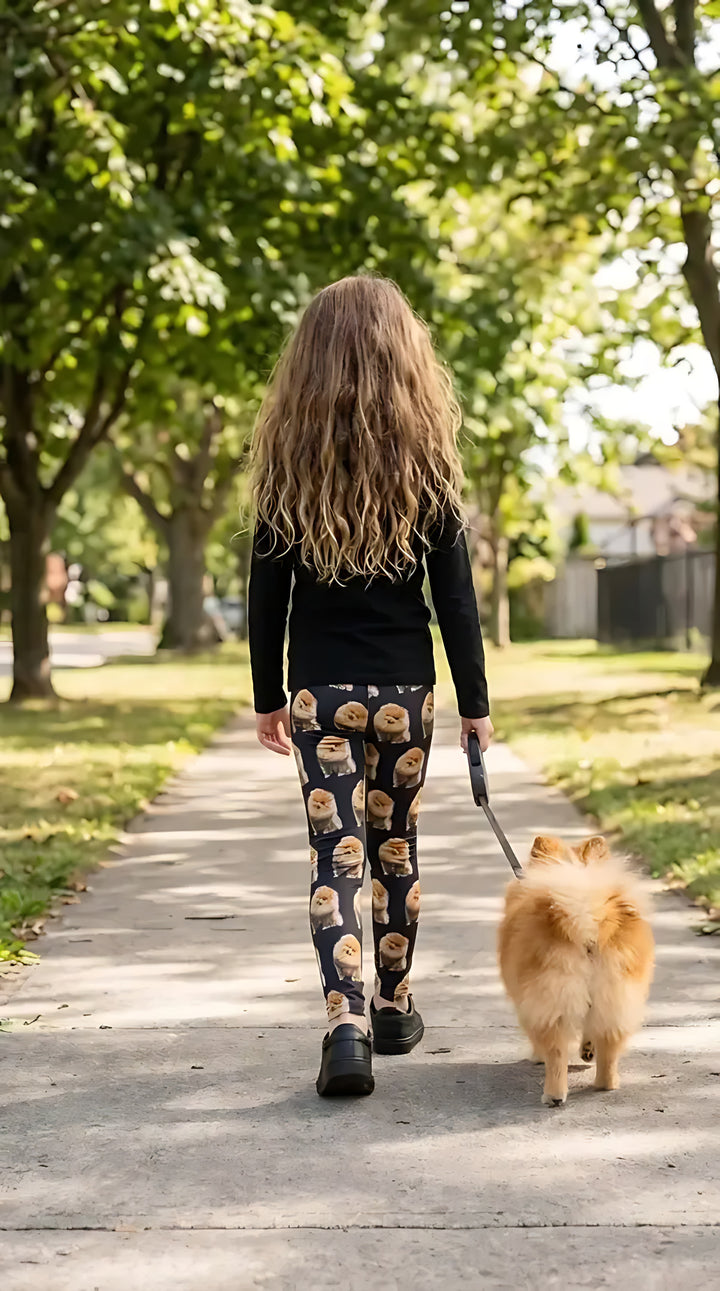 Back view of a girl walking a Pomeranian on a tree-lined sidewalk, wearing black Pomeranian print girls leggings