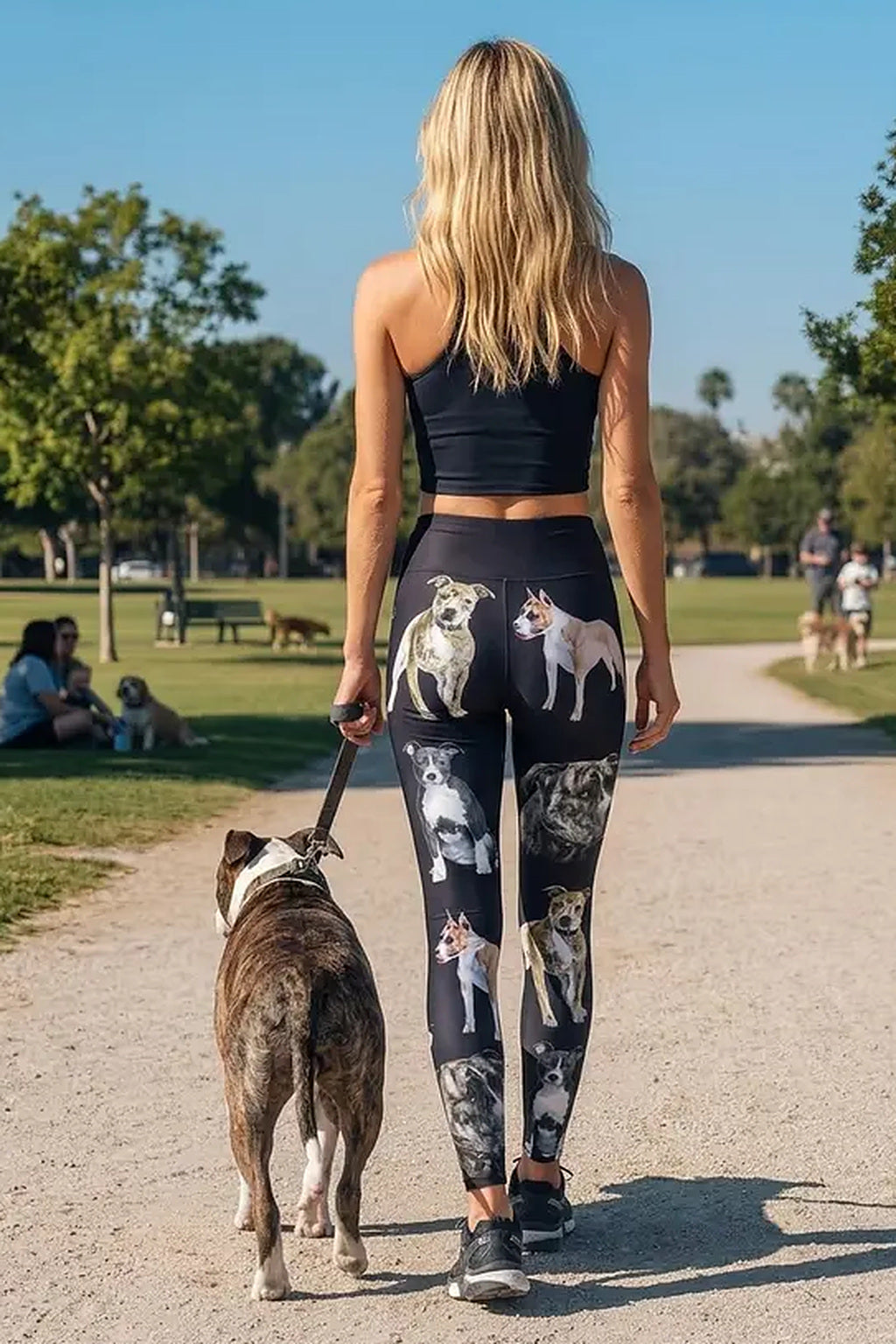 Back view of a woman walking a brindle pit bull on a park path in black pit bull print leggings