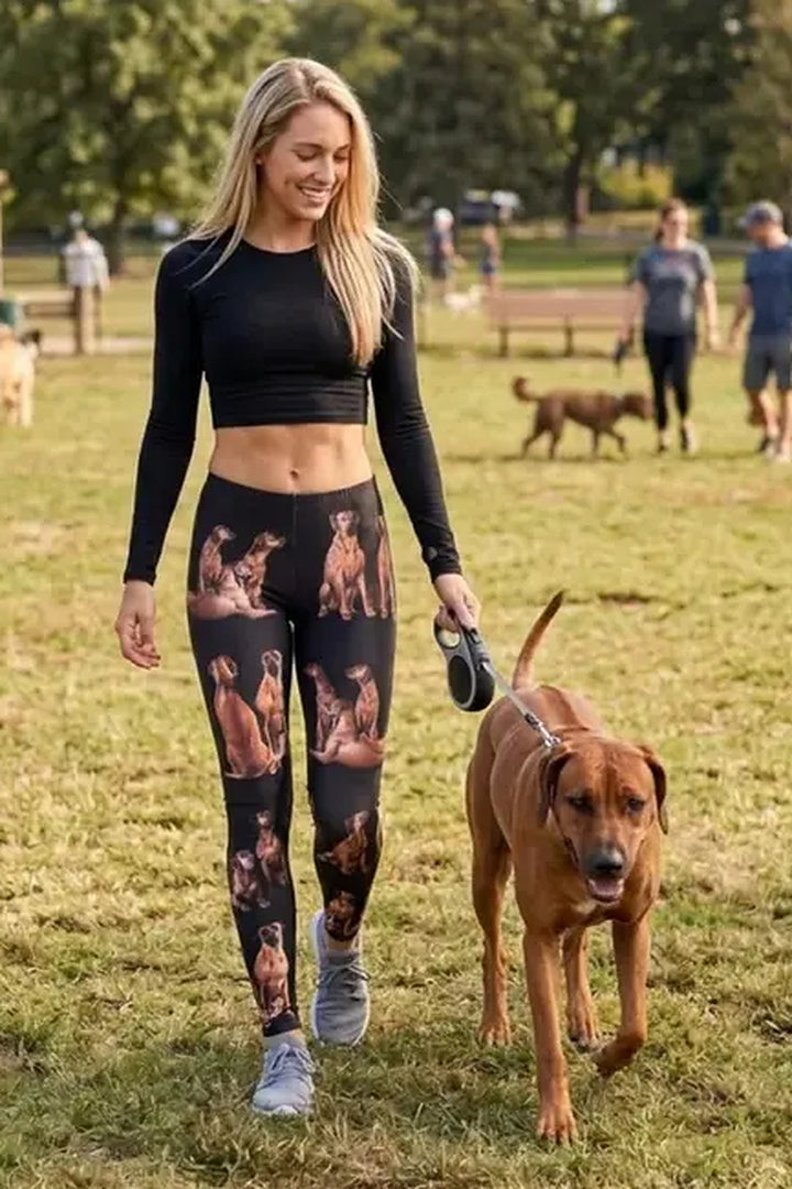 Woman in a black crop top walking a Rhodesian Ridgeback in a park, wearing ridgeback print leggings